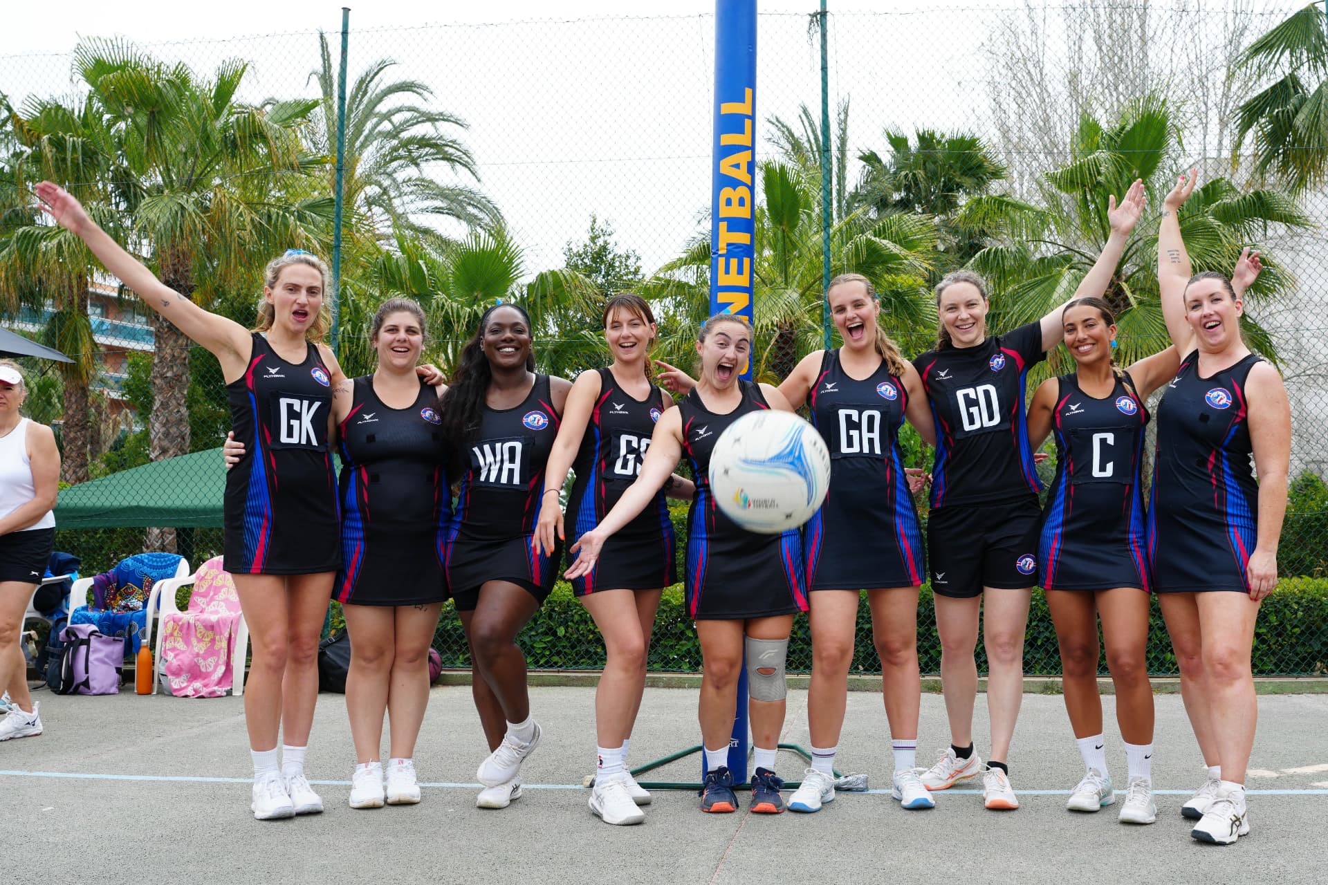 Barcelona Netball Club players celebrating together in their match kit by the netball post